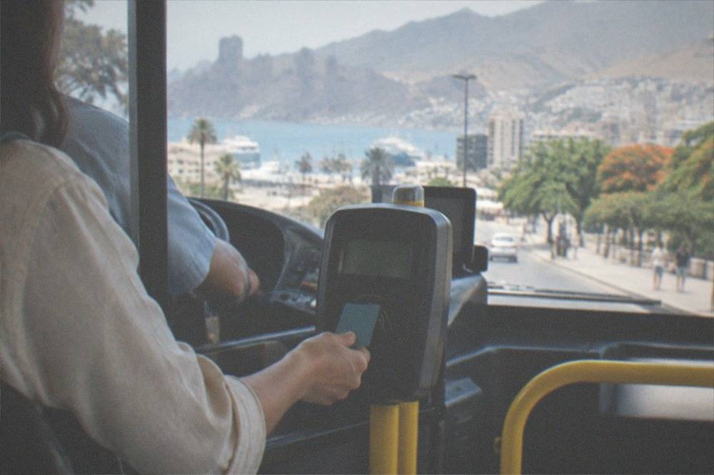 A passenger tapping a travel card on a bus validator beside the driver