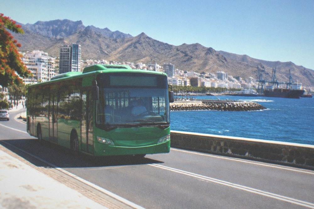 A green bus travelling a coastal road with the sea on one side