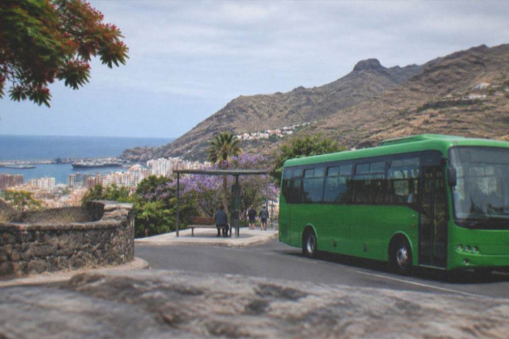 A green bus parked at a mountain village stop with terraced slopes behind