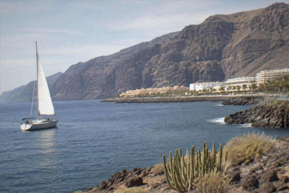 A sailboat on calm water near tall cliffs on the Tenerife coast