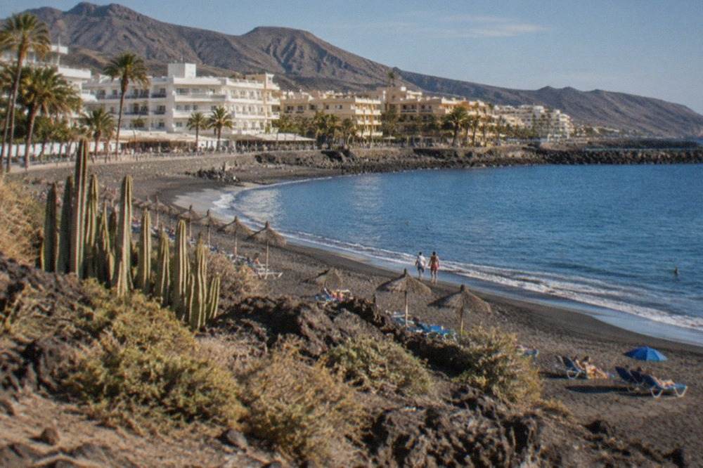 A sunny beach in south Tenerife with calm blue water and parasols in August