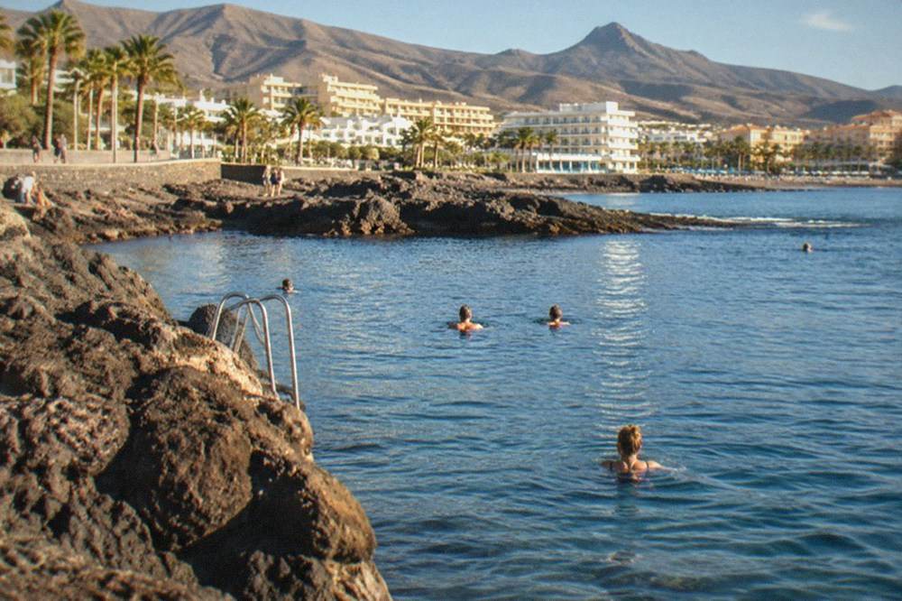 Swimmers in calm blue water beside a volcanic rock bay in Tenerife
