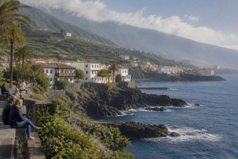 Visitors sitting in sunshine on a seafront promenade in South Tenerife
