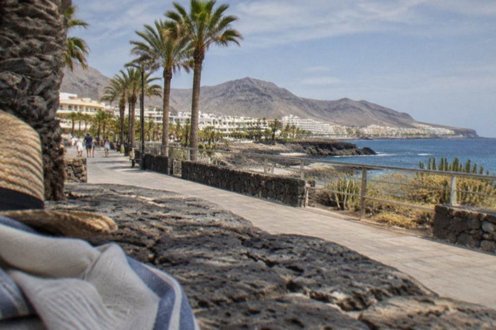 A shaded seafront promenade in a Tenerife resort town under strong midday sun