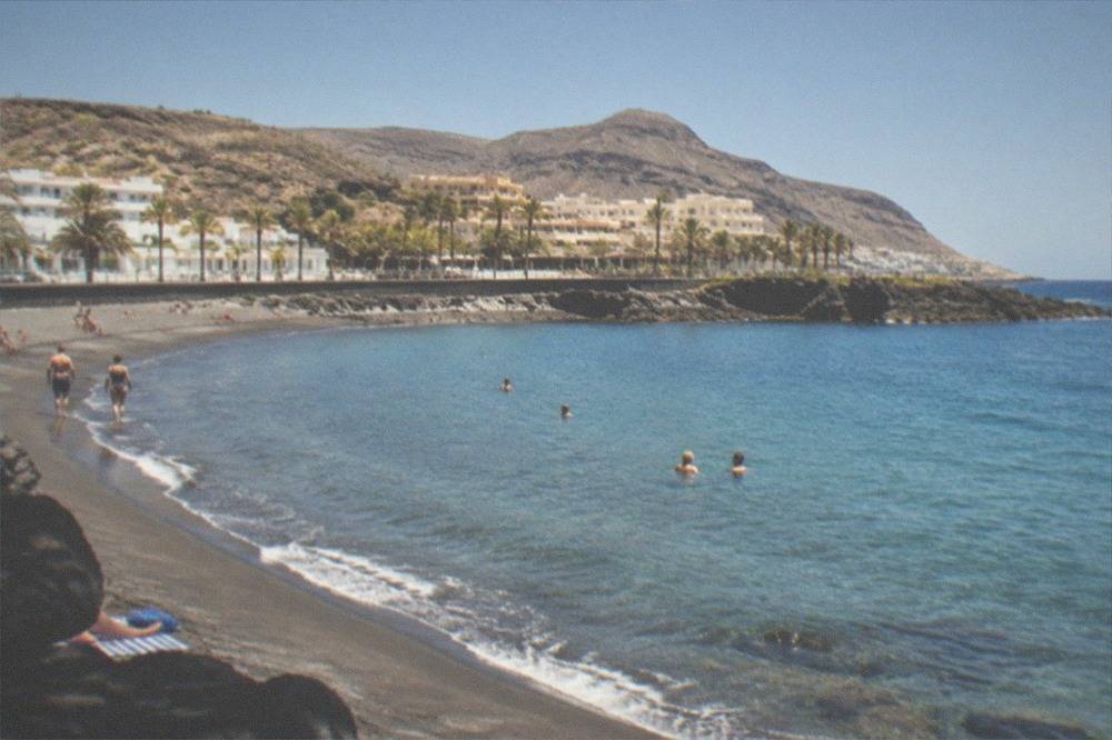 People swimming in clear turquoise water at a Tenerife beach