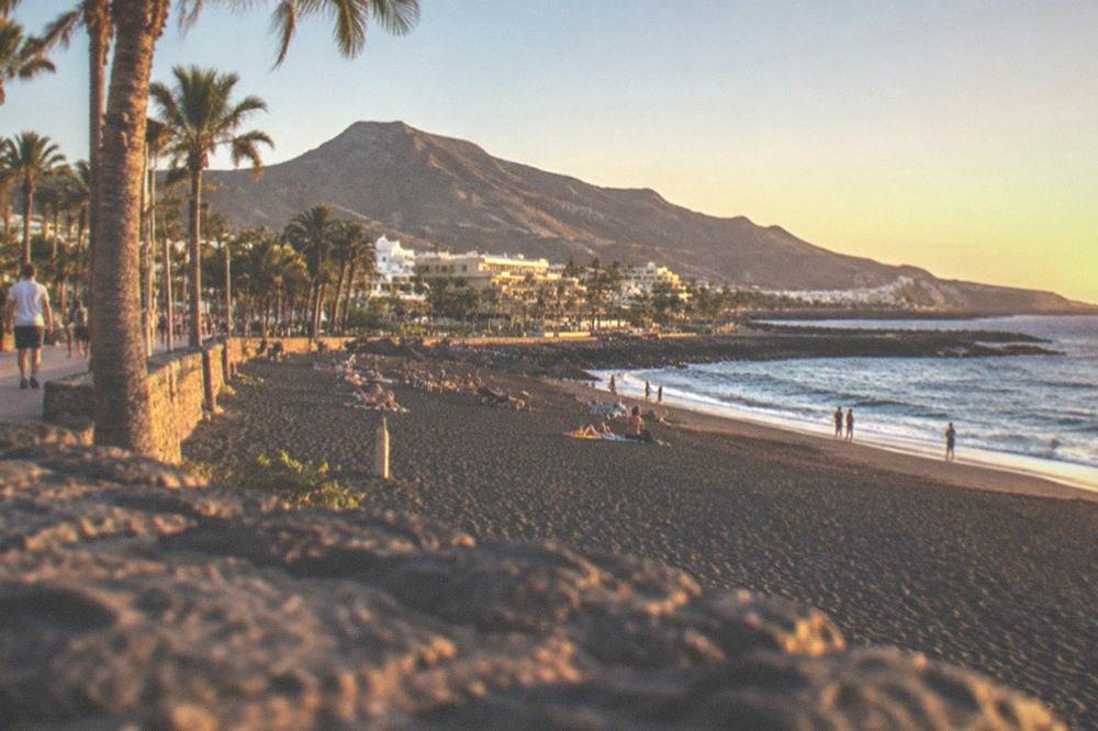 A busy beach promenade with palm trees in a Tenerife resort in summer