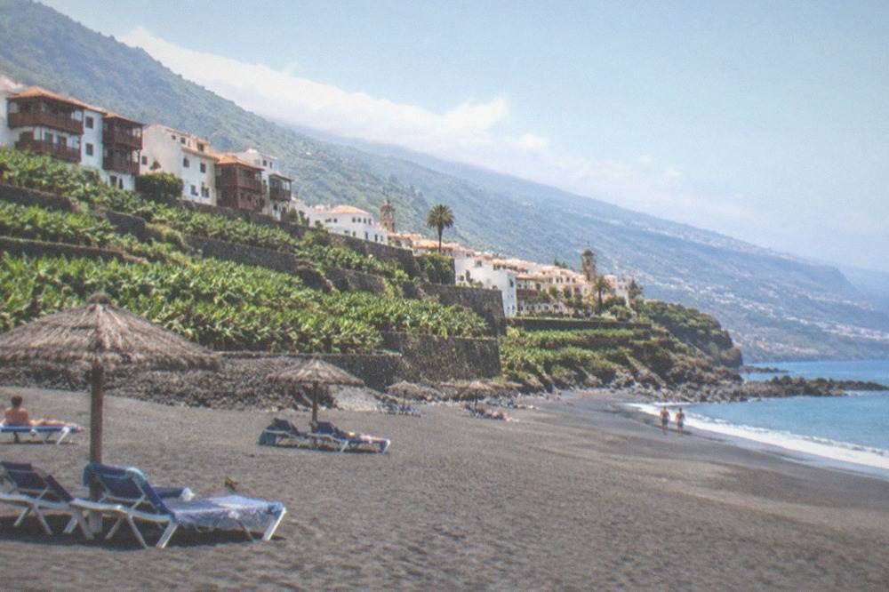 Sun loungers on a pale sandy south Tenerife beach with a clear sky and calm water