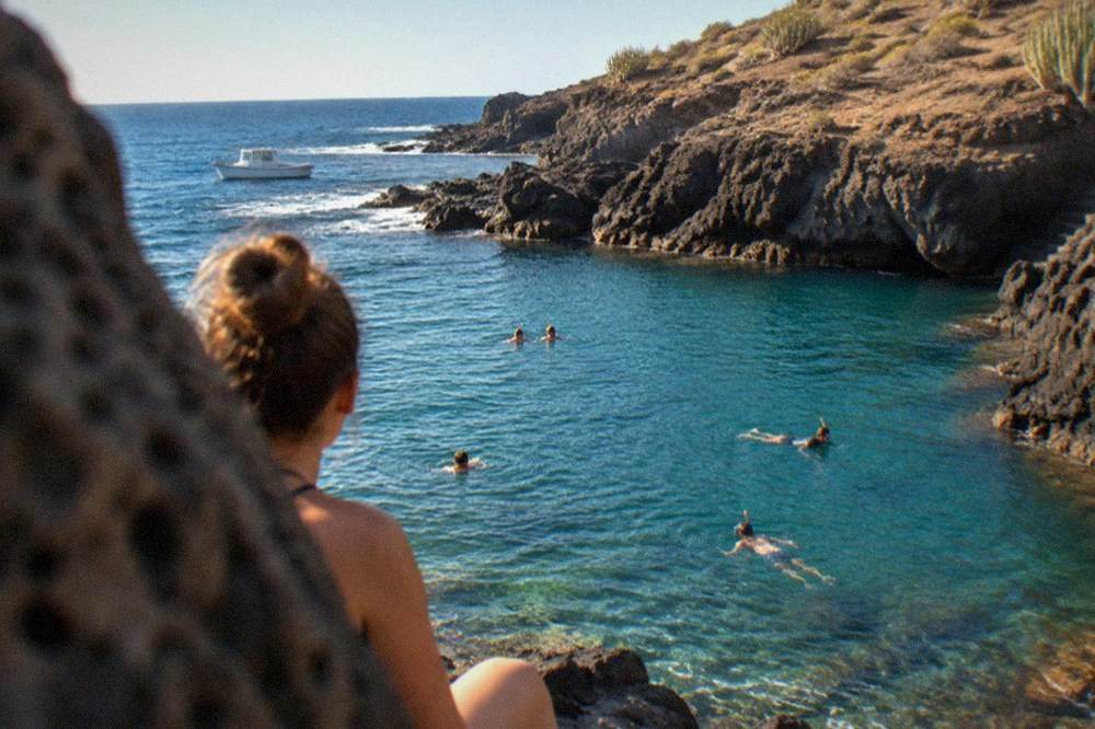 People swimming and snorkelling in clear turquoise water near the rocky cove at El Puertito