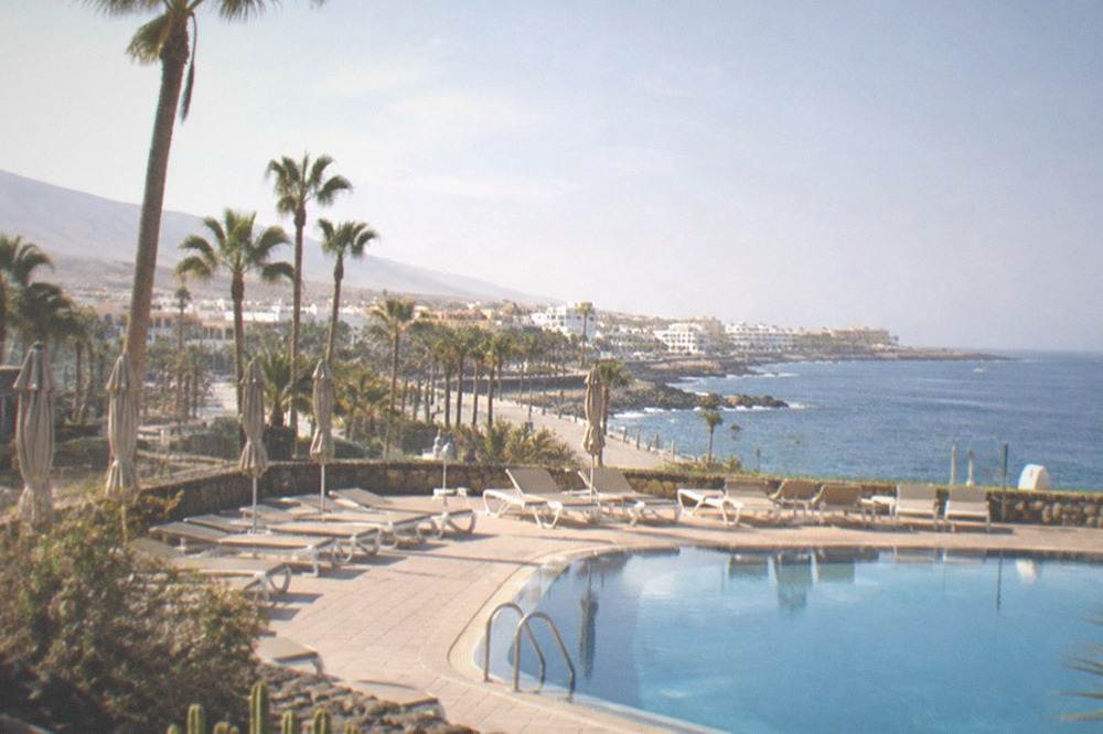 An empty sunlounger-lined hotel pool terrace at Costa Adeje with palm trees and a sea view