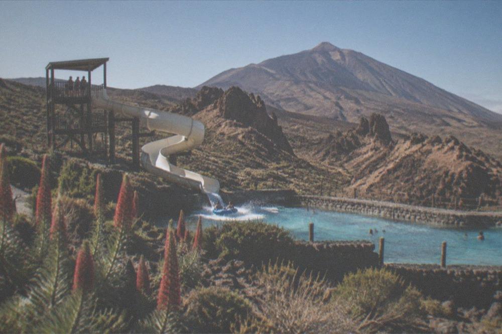 A water park slide tower with people on rafts splashing into a lagoon under sunshine