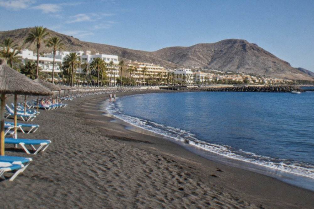 A sunny beach at Los Cristianos with sunbeds and calm water in late autumn