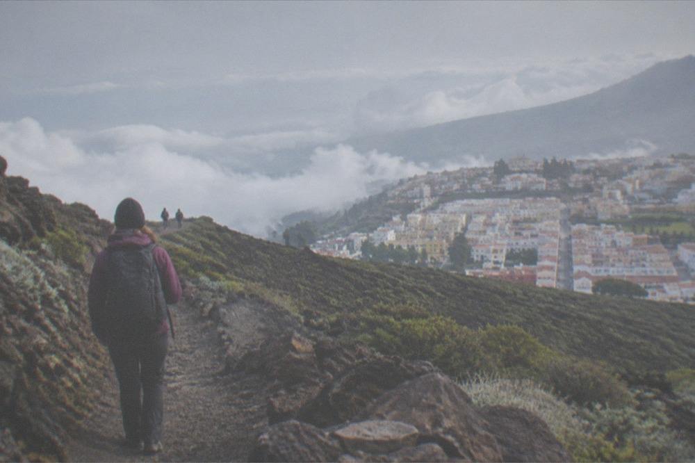 A hiker in warm clothing on a rocky volcanic trail above the clouds