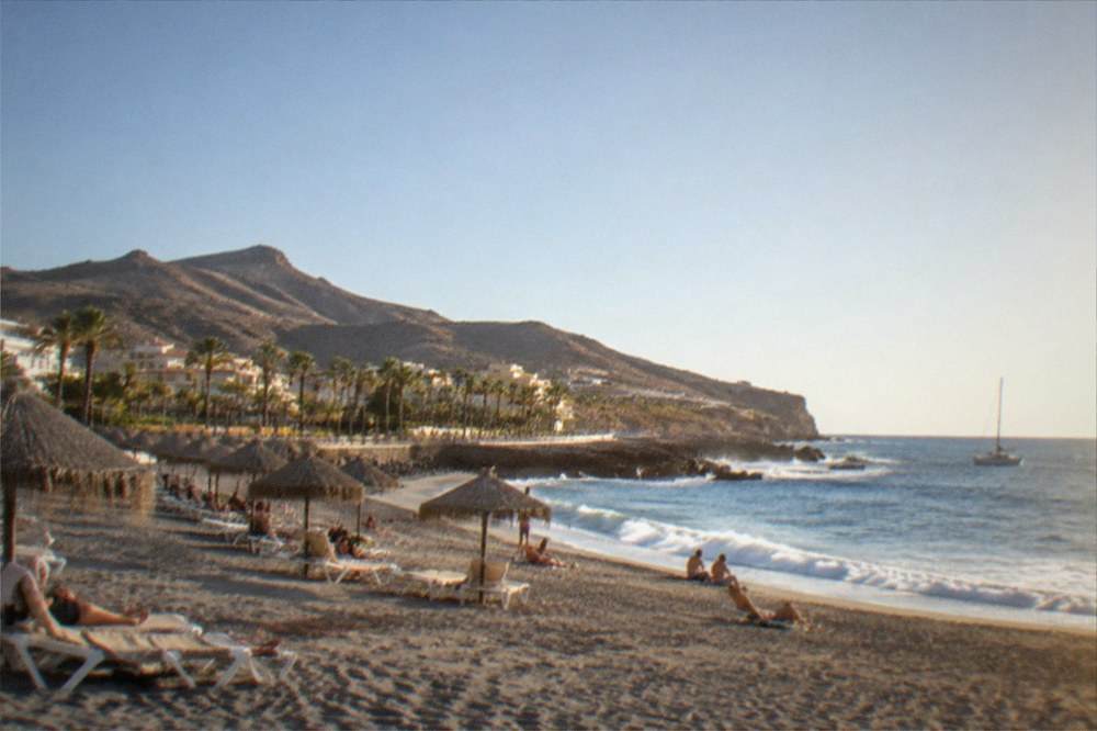 Sunbeds and parasols on the sandy beach at Playa del Duque with people relaxing in the sun