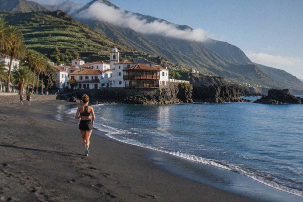 A sunny beach in south Tenerife with calm water and palm trees under a clear sky