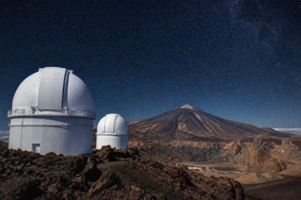 White telescope domes of the Teide Observatory on a rocky ridge under a clear sky