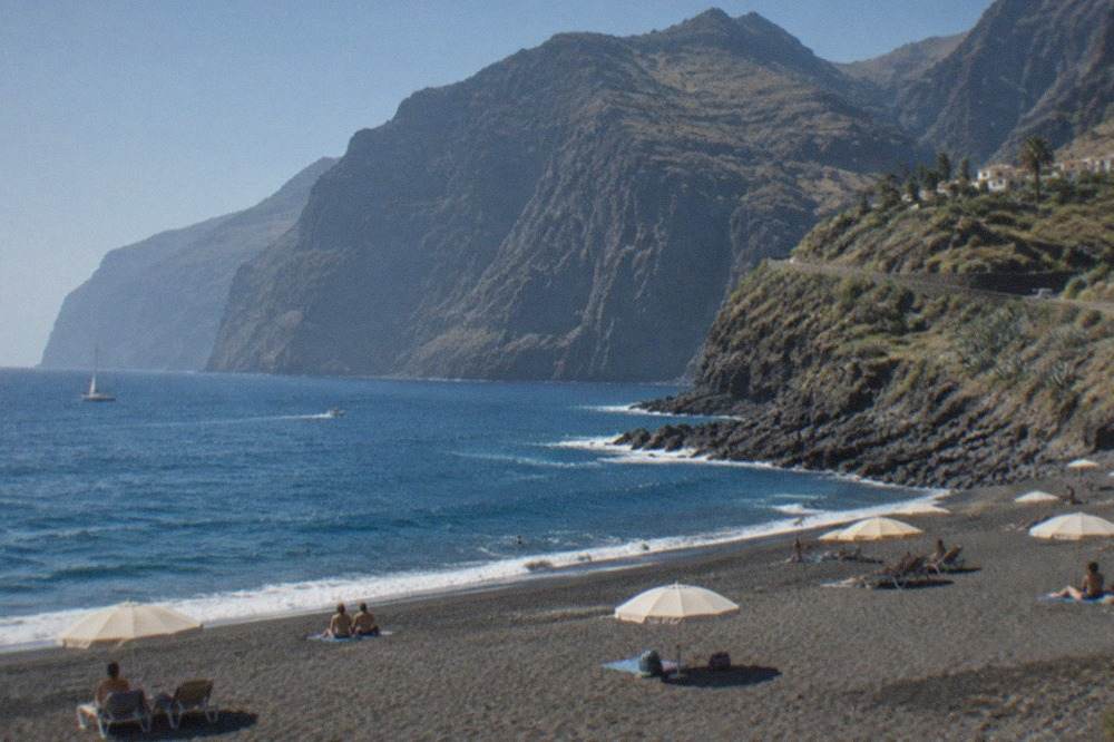 A calm south Tenerife beach under a clear blue sky with sun umbrellas on golden sand