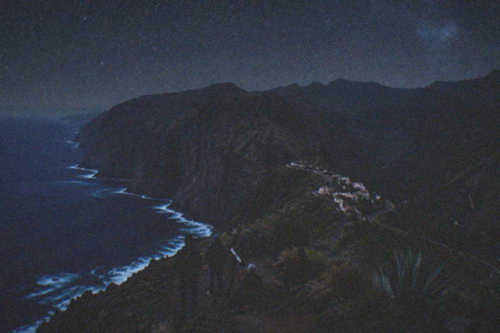 A stargazing group with a telescope on a dark mountain ridge under a starry sky