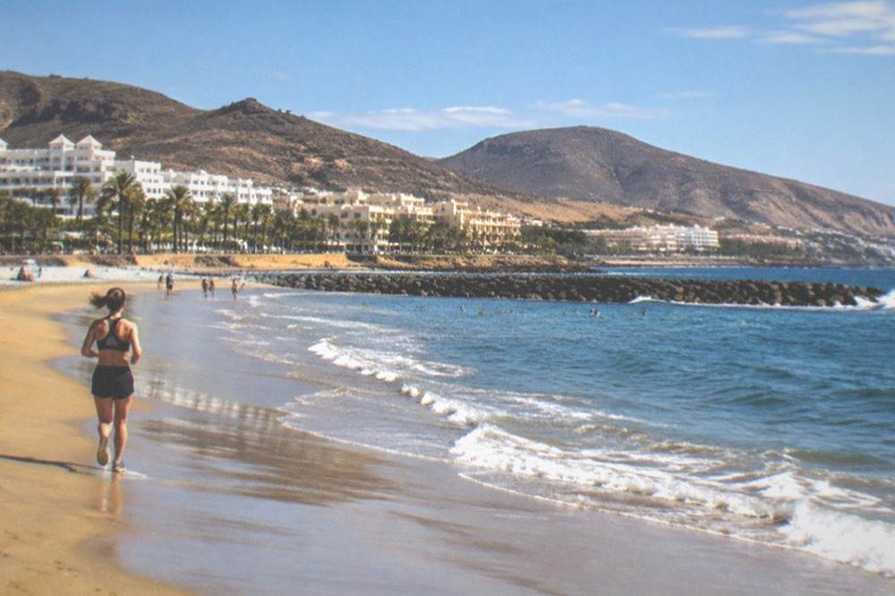 A sheltered golden-sand beach at Playa de las Vistas with breakwaters and resort buildings behind it