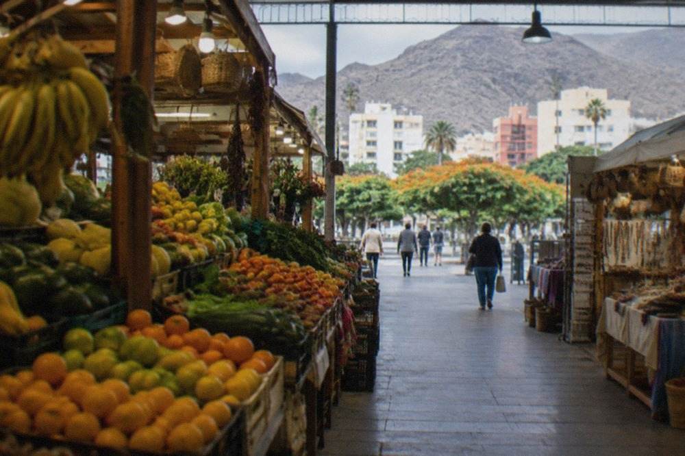A covered market hall in Tenerife with stalls of fruit, vegetables and handmade goods under warm lighting