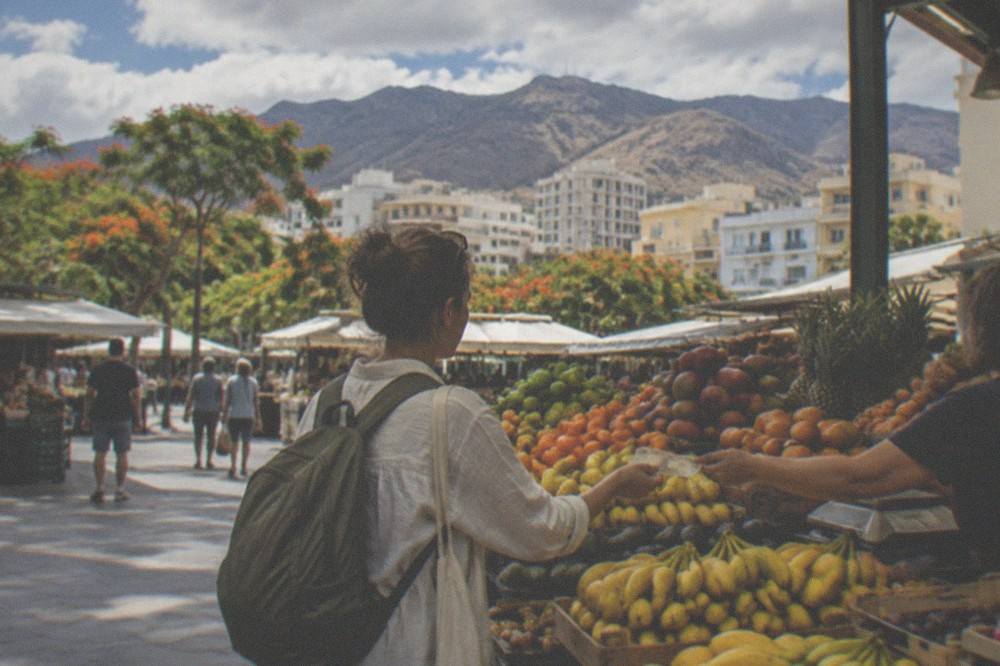 A visitor browsing a fruit stall and handing over euro notes at a Tenerife market