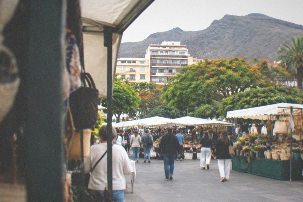 A busy open-air market square in Tenerife with visitors browsing covered stalls
