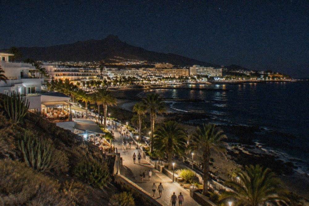 A lit promenade in a Tenerife resort town at night with people walking between bars and restaurants