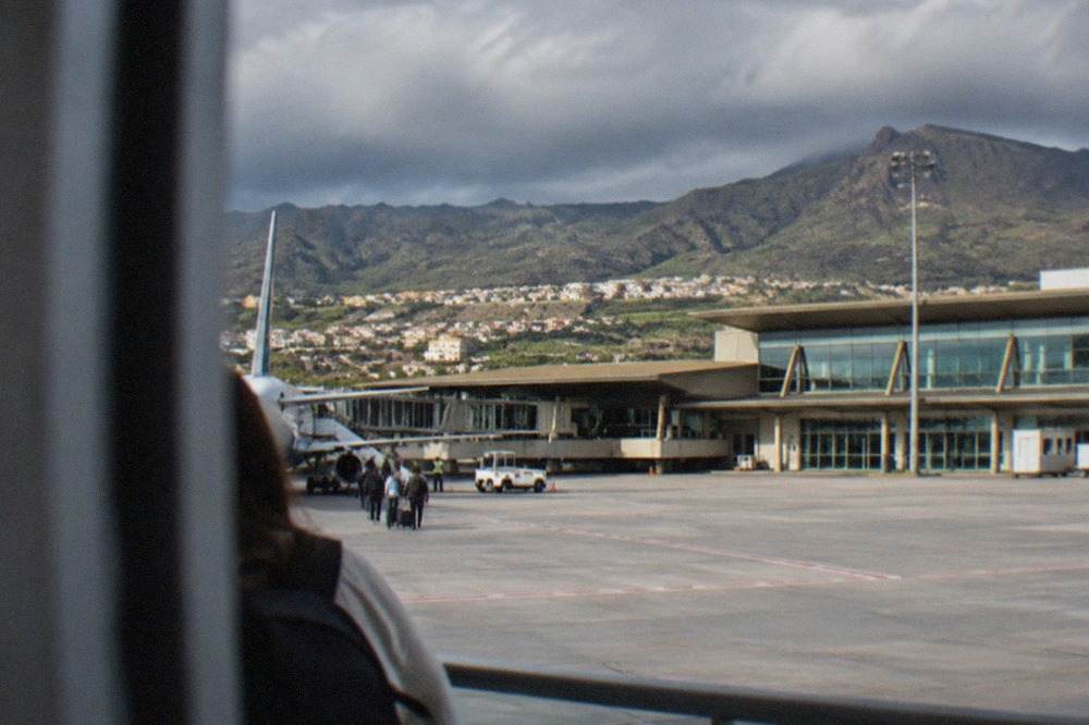 A passenger terminal building at Tenerife North Airport with volcanic hills behind it under a cloudy sky