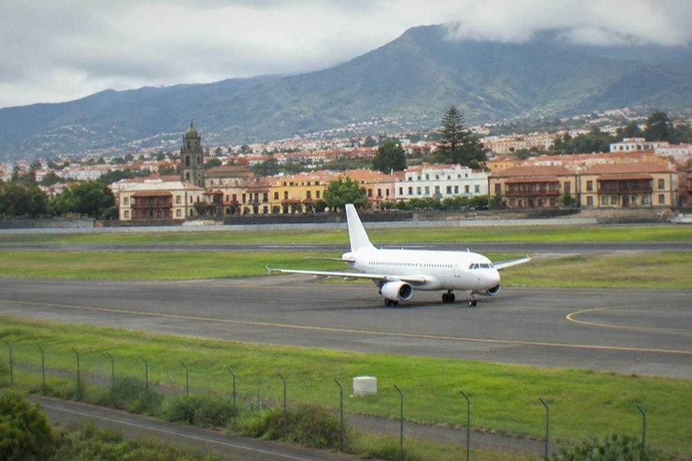 A white passenger aircraft taxiing at a green island airport with mountains in the distance