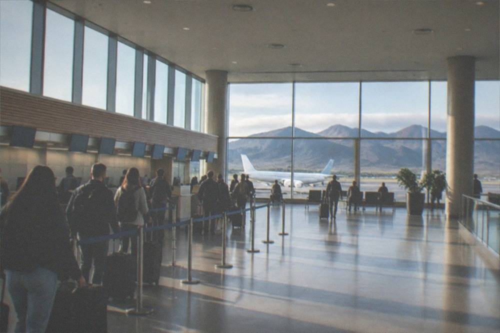 A departure hall with check-in desks and a queue of travellers with suitcases