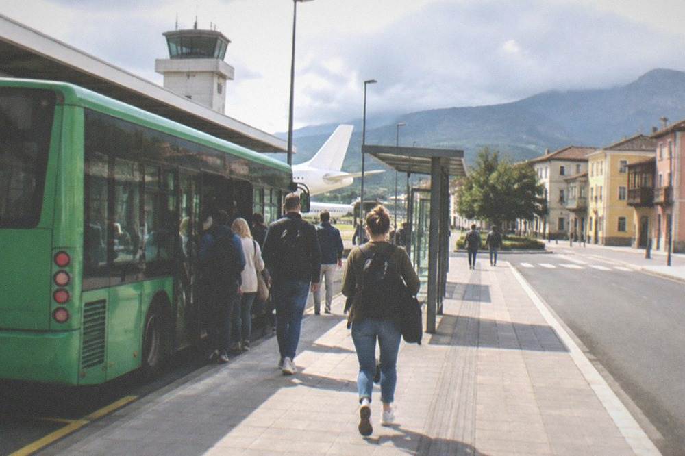 A green island bus at an airport stop with passengers boarding