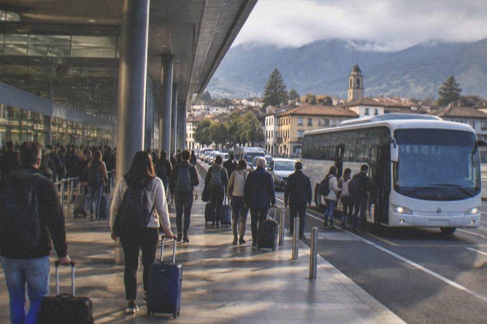 A crowded airport arrivals hall with travellers queuing at a bus stop outside
