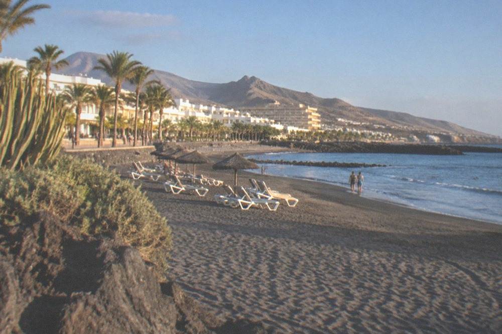 Grey sand beach with sun loungers and calm water at a Costa Adeje seafront