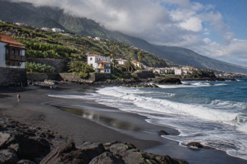 A wide view of dark volcanic sand and rolling Atlantic waves on a quiet Tenerife morning