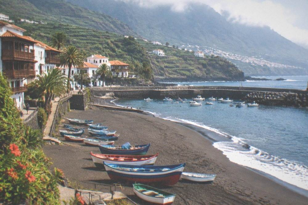 Colourful fishing boats resting on the sand beside a small southern Tenerife harbour at midday