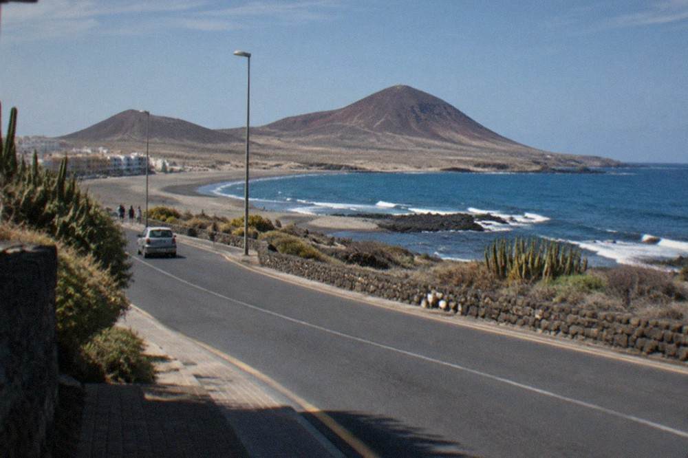 A road through El Medano on the dry southern side of Tenerife with volcanic hills in the background