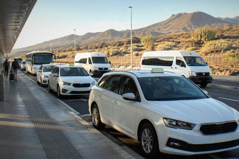 A row of white taxis and shuttle minibuses waiting at an airport kerbside