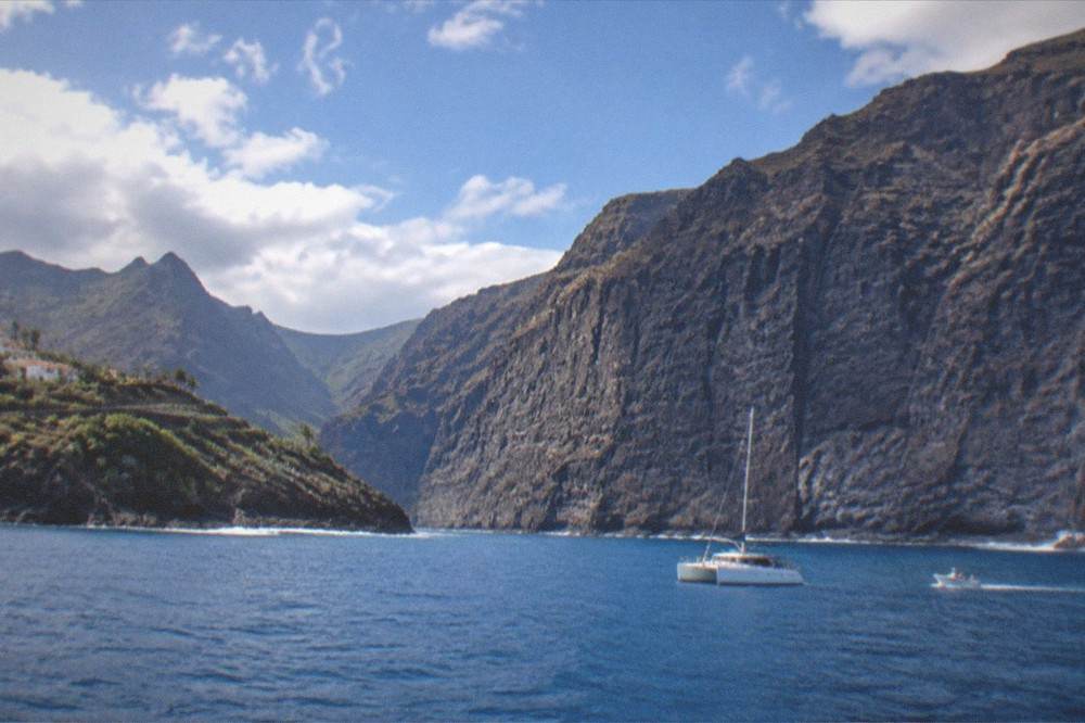 A catamaran and a small boat on calm blue water near the cliffs of Los Gigantes