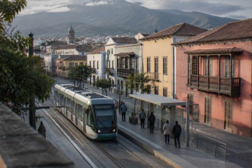 A tram arriving at a platform with mountains behind La Laguna