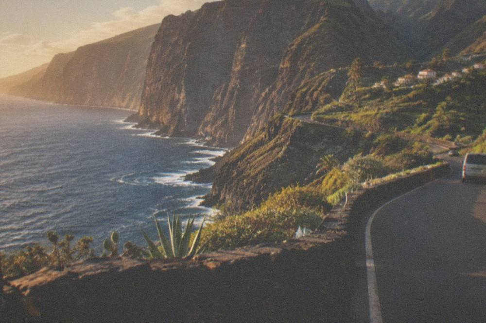 A coastal road curving along cliffs with the ocean on one side and green hills on the other