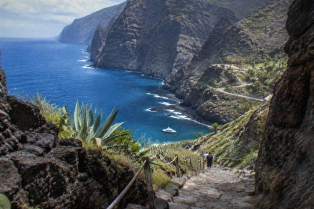 A narrow rocky gorge path descending towards a small bay with a boat
