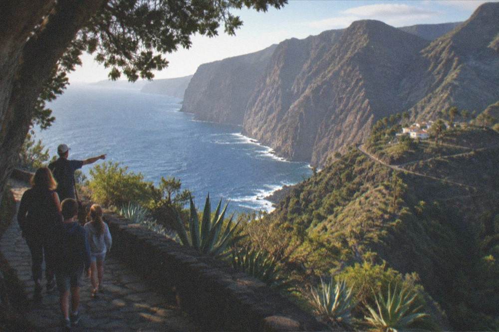 A family walking a paved path beside a tall tree with a guide pointing ahead