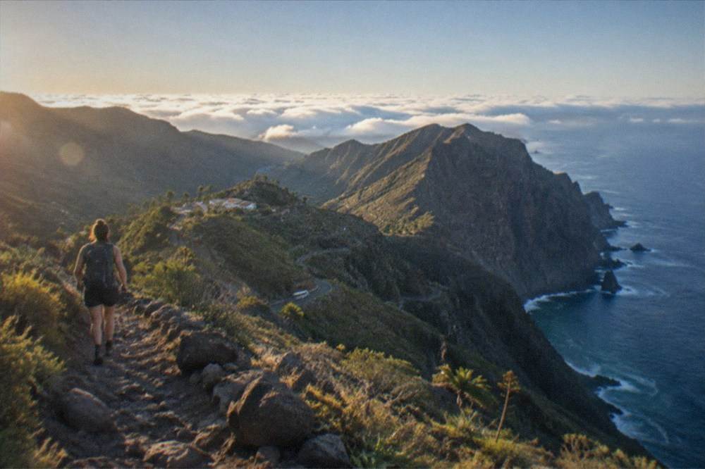 A hiker with a backpack on a stony mountain trail above a sea of clouds