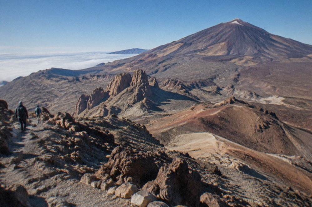 A volcanic mountain ridge rising above a layer of clouds under a blue sky