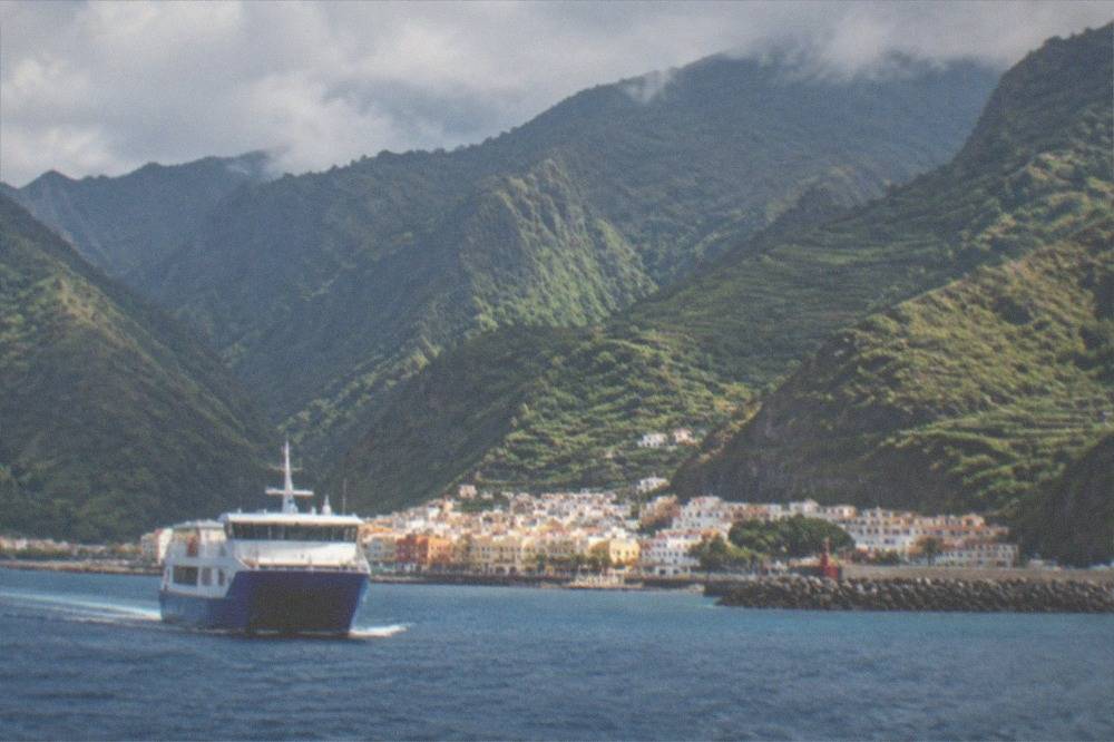 A blue ferry approaching San Sebastian de la Gomera with green mountains behind it