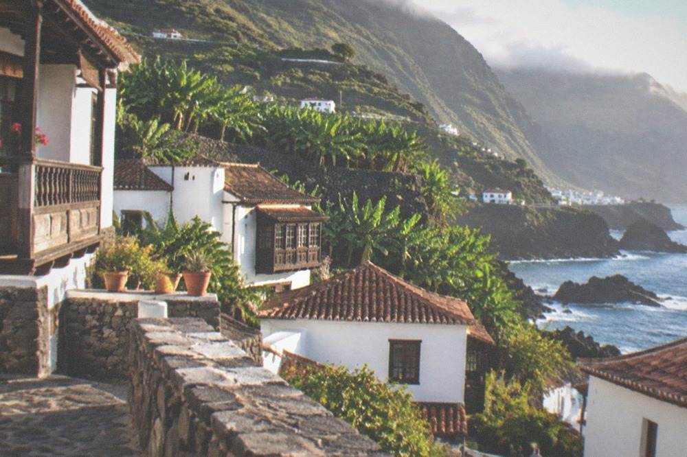 A stone terrace of small white houses in Garachico on a green hillside above the sea