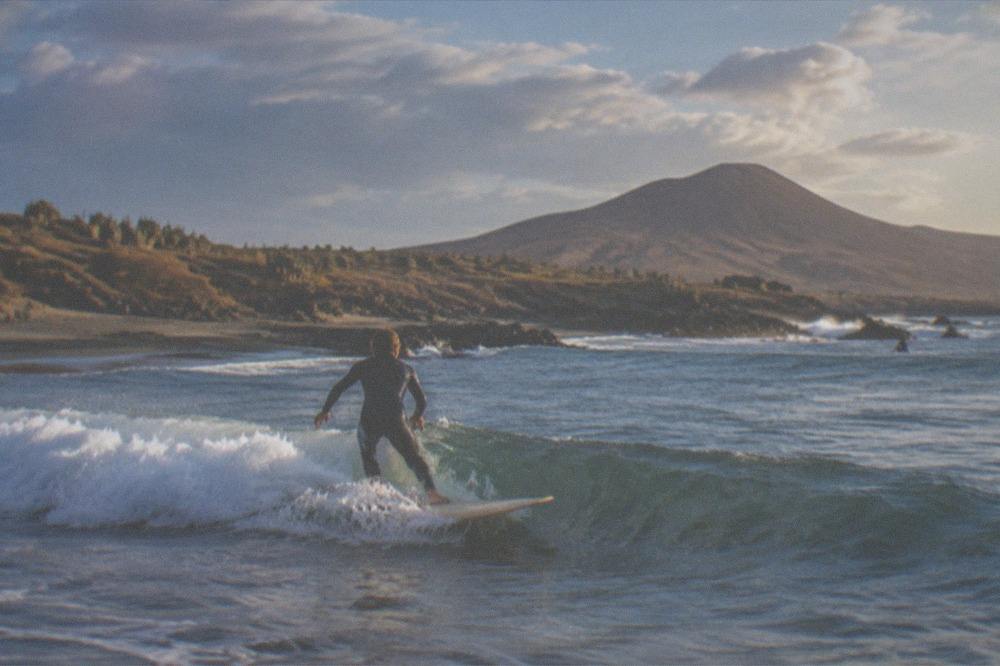 A person on a surfboard riding a small wave at El Medano in warm evening light