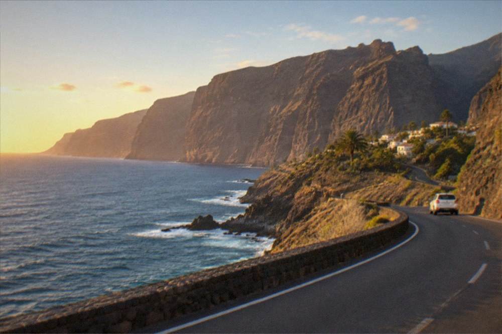 A coastal road at Los Gigantes winding between dark volcanic rock and the blue ocean