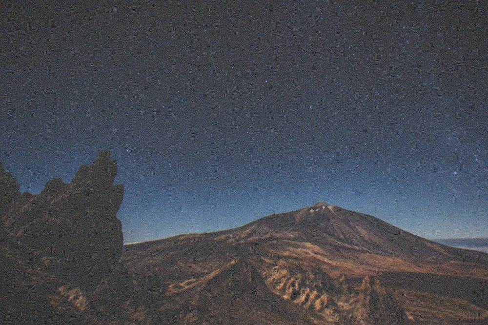 A starry night sky above silhouetted volcanic rocks at high altitude