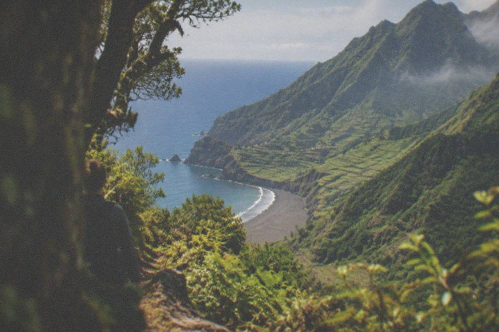 Two contrasting island landscapes side by side, a golden beach with calm water and a green cliff terraced with fields