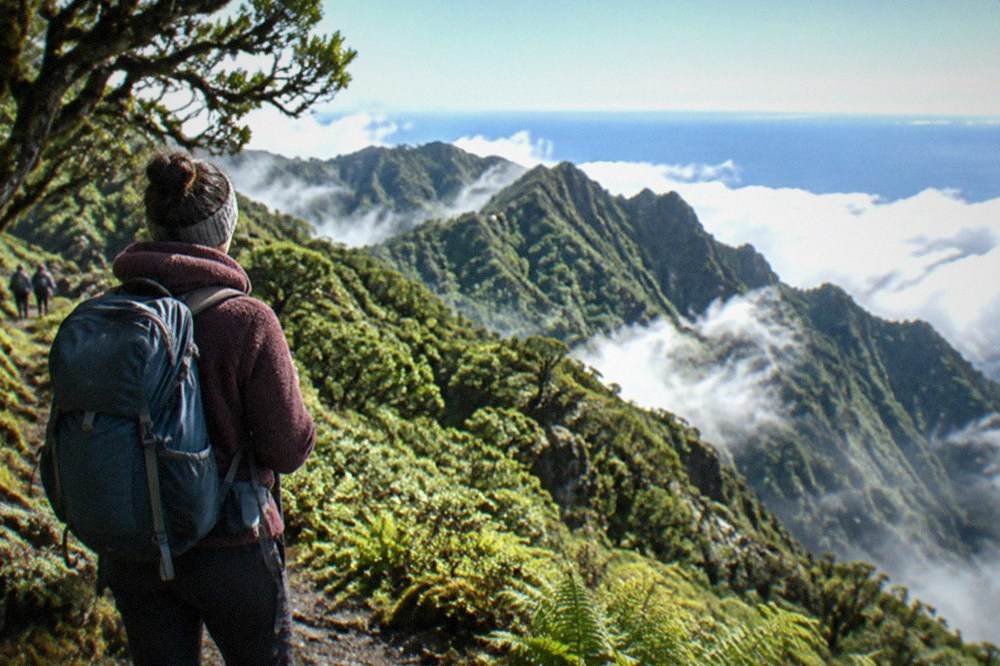 A hiker in warm clothing on a high volcanic ridge above a sea of clouds